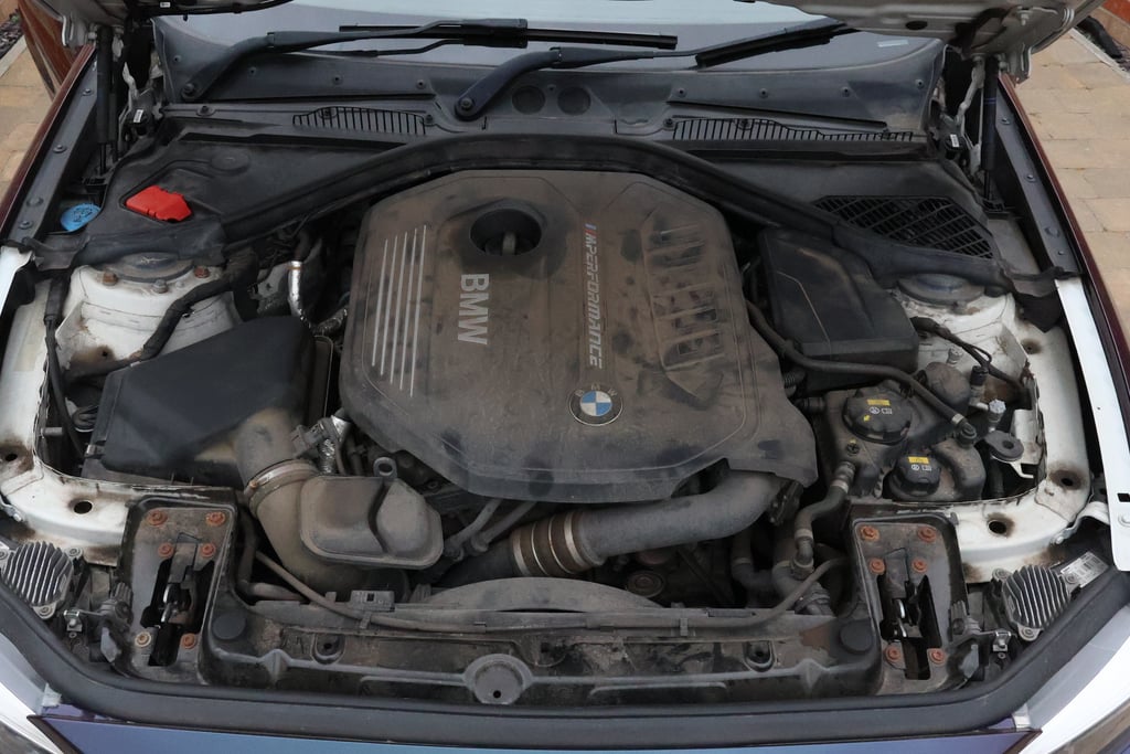 BMW B58 engine bay before cleaning, every surface grey with road dust and oil mist