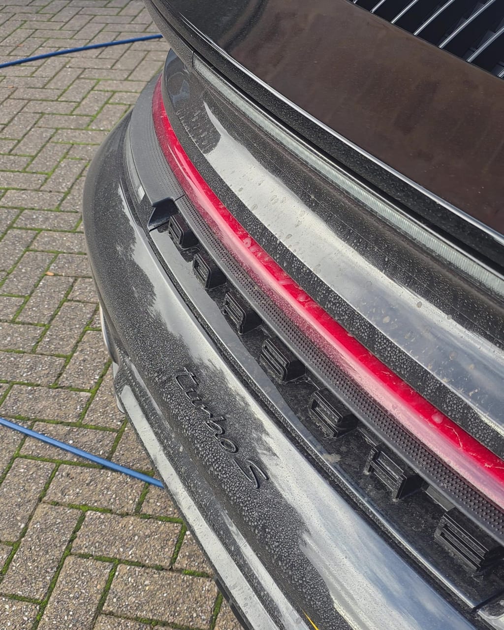 Rear bumper and diffuser of a black Porsche 911 Turbo S before cleaning, lettering and vents filmed with road dirt