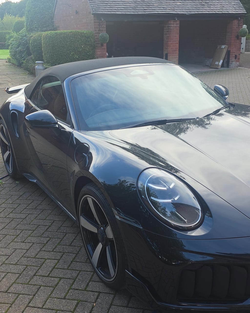 Black Porsche 911 Turbo S front three-quarter before a maintenance valet, paint dulled by two weeks of road film