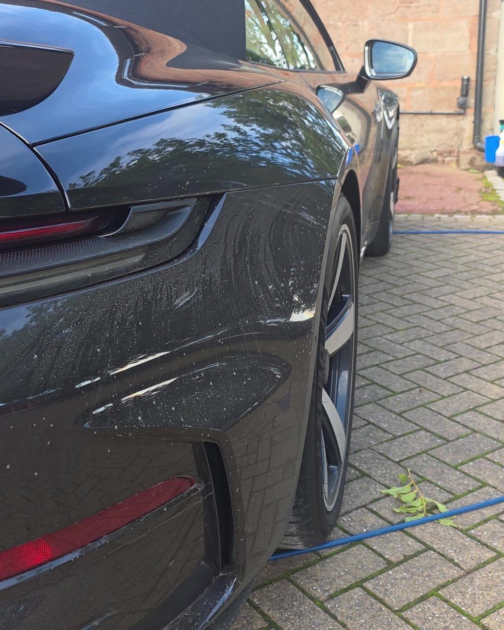 Rear quarter panel of a black Porsche 911 Turbo S before its valet, water spotting visible across the paint