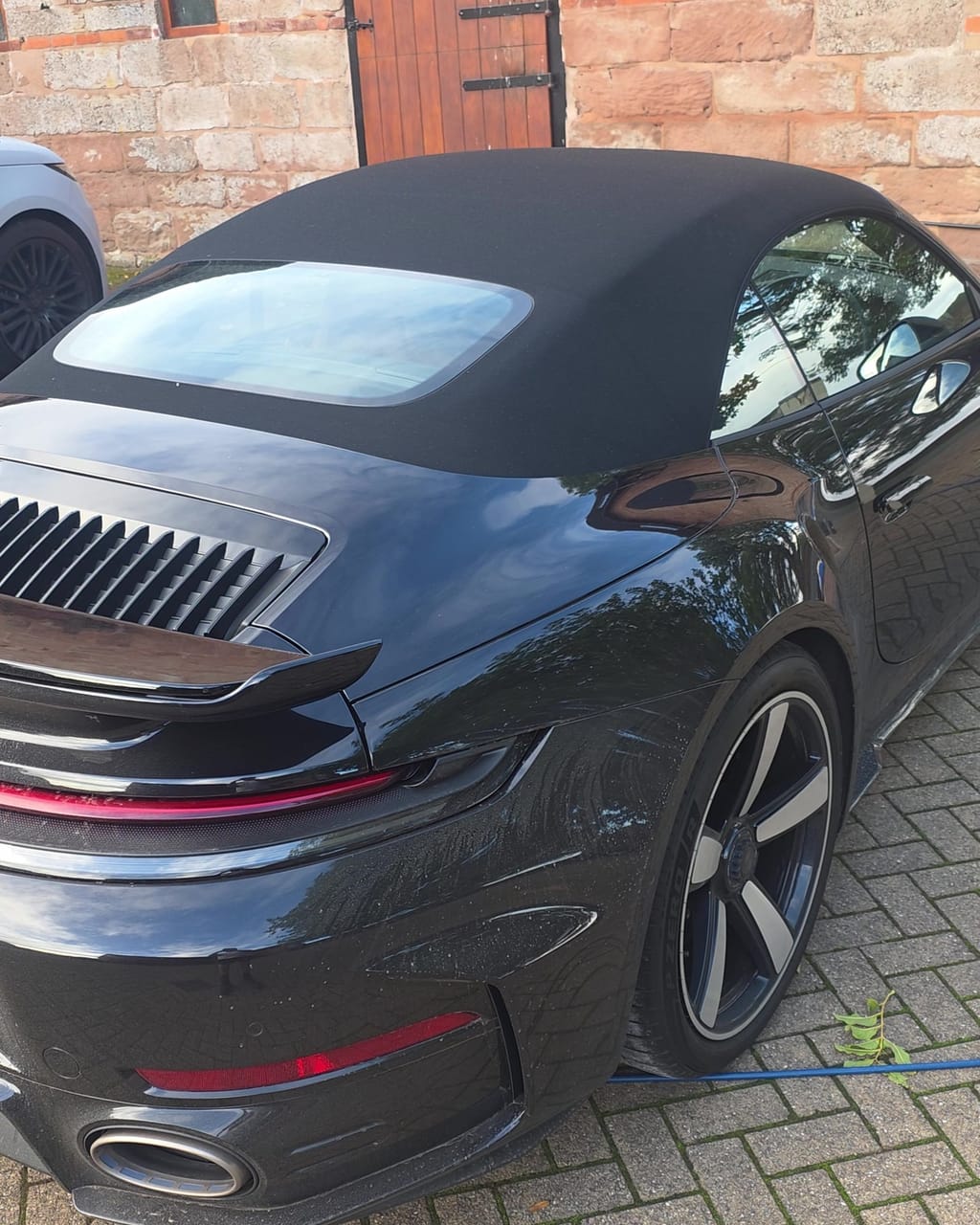 Rear three-quarter of a black Porsche 911 Turbo S before its maintenance valet, engine lid dusty and reflections broken