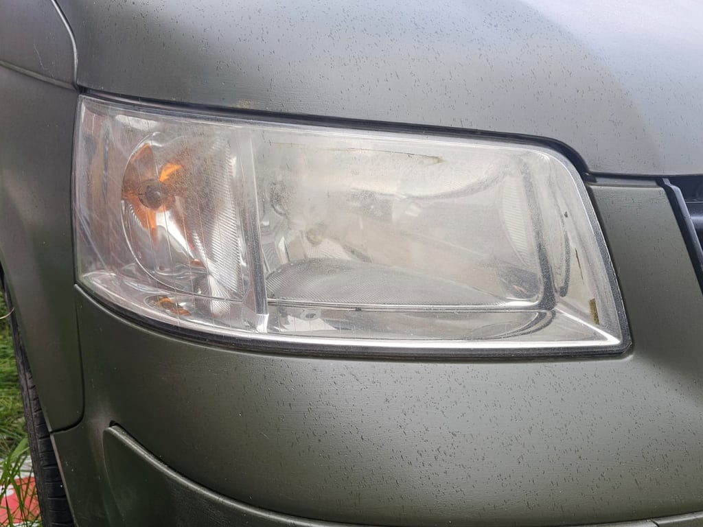 The same VW Transporter T5 headlight before restoration, the lens hazy and yellowed so the reflector behind it is barely visible