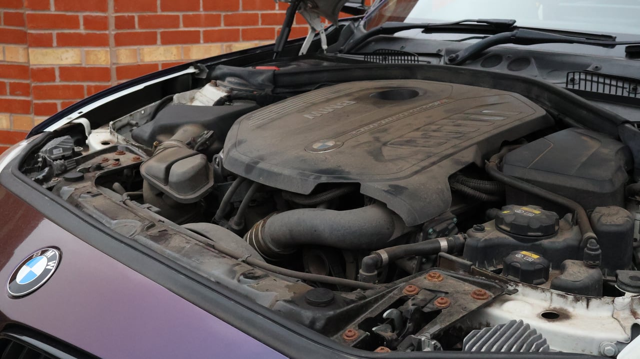 BMW engine bay before cleaning, thick with road dust and oil mist