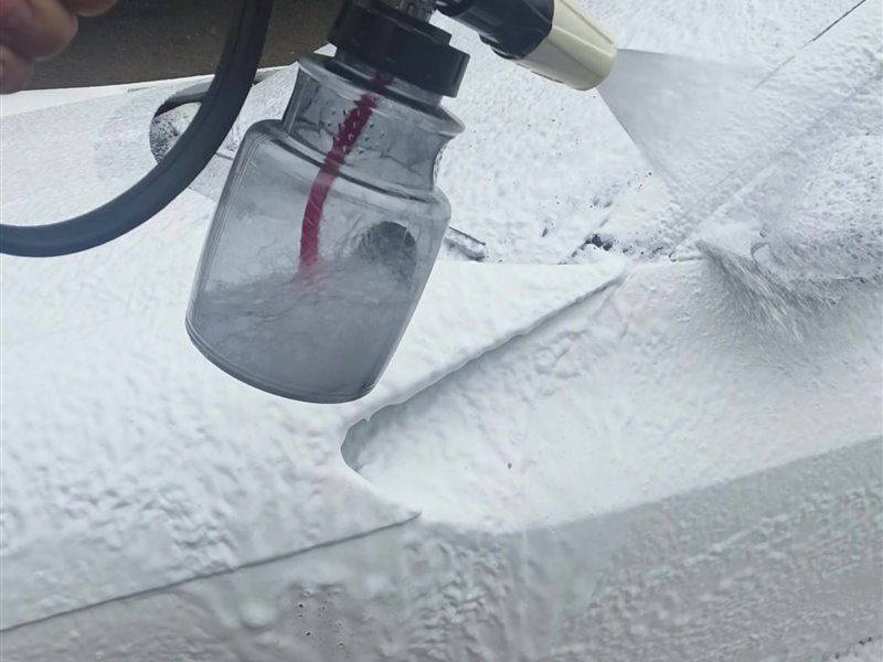 Snow foam being applied to a white Ferrari Purosangue with a foam lance