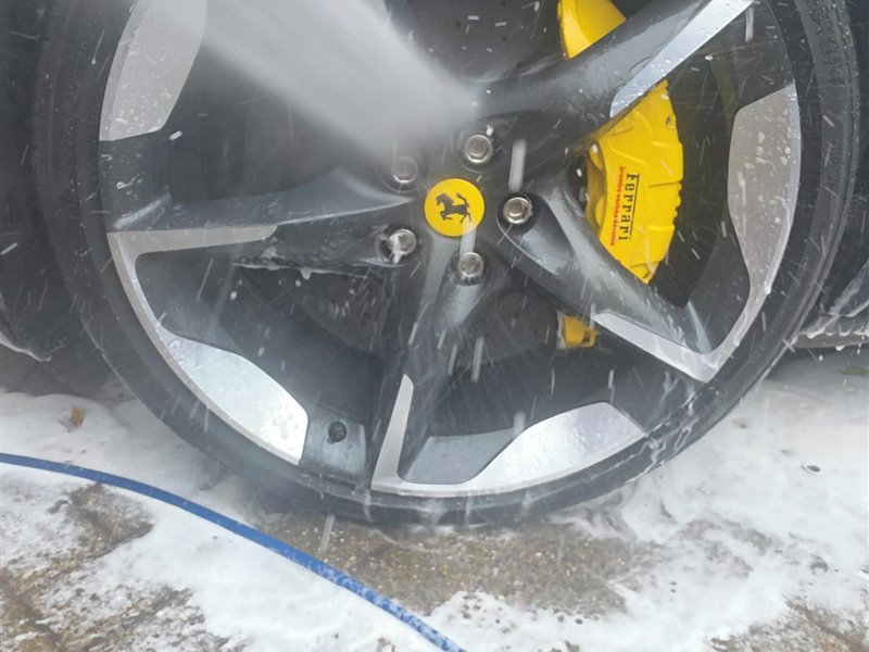 Ferrari Purosangue forged wheel and yellow brake caliper being rinsed clean