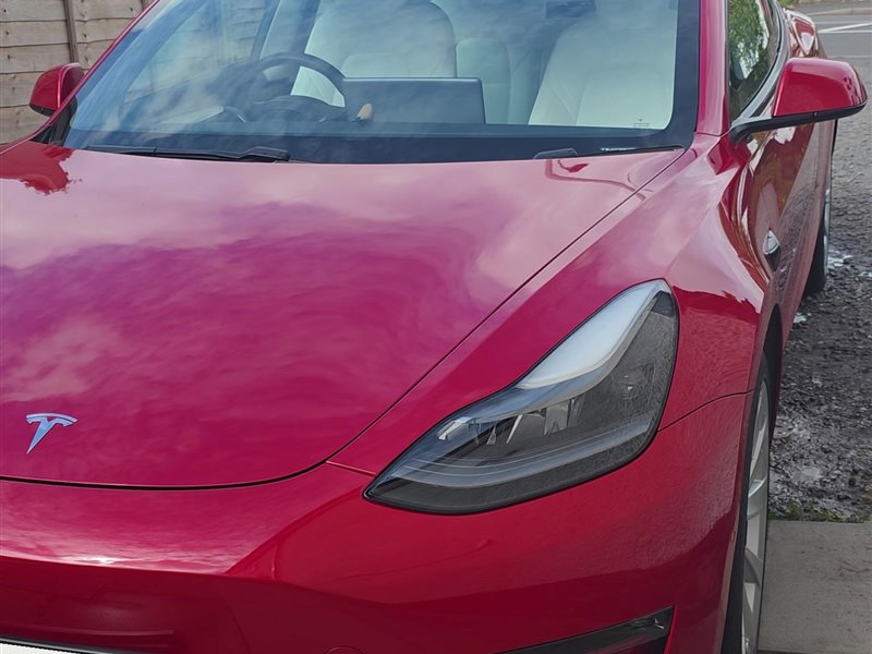 Red Tesla Model 3 headlight and front wing after detailing